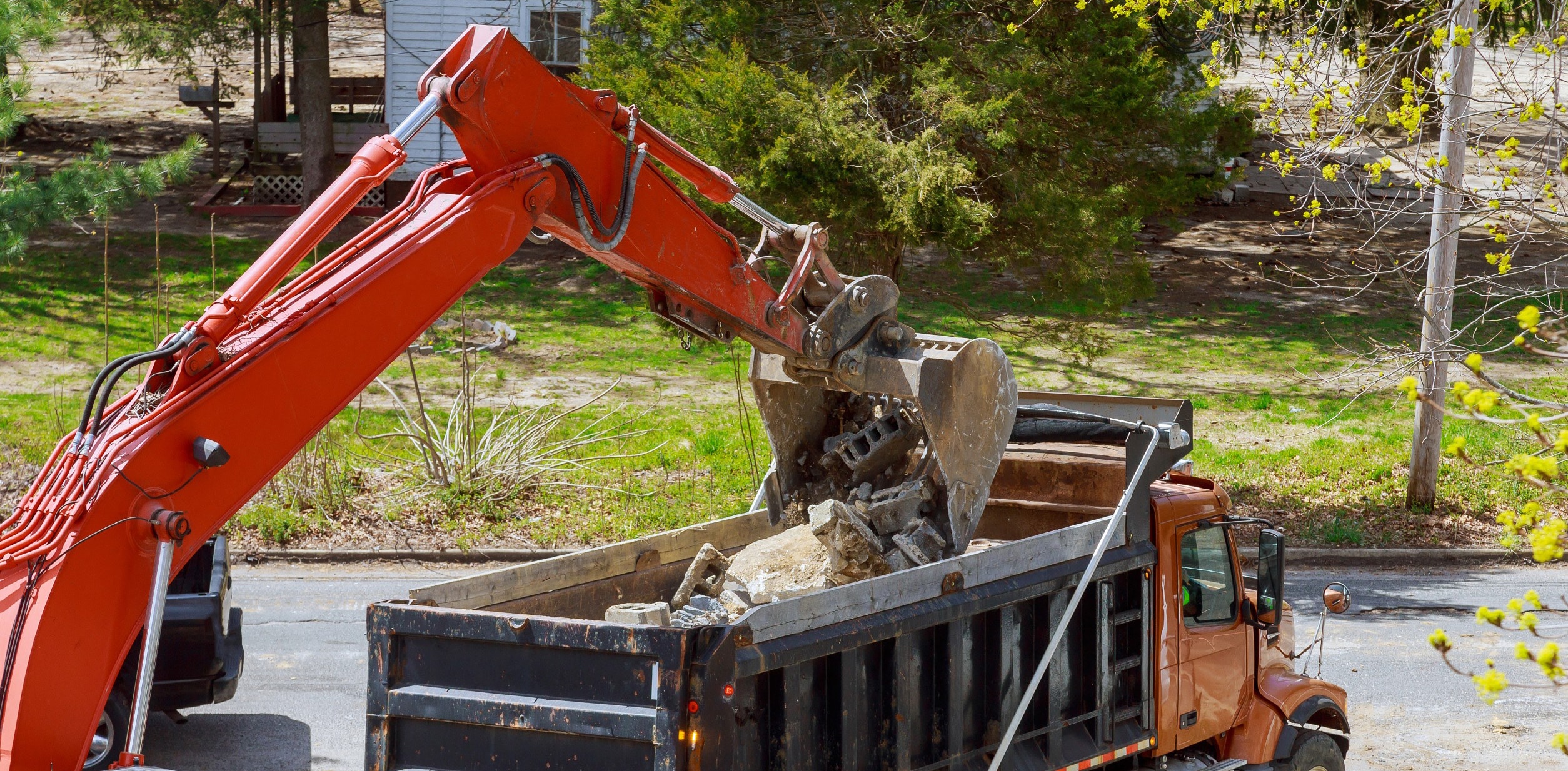 Excavator loading demolition debris into a dump truck