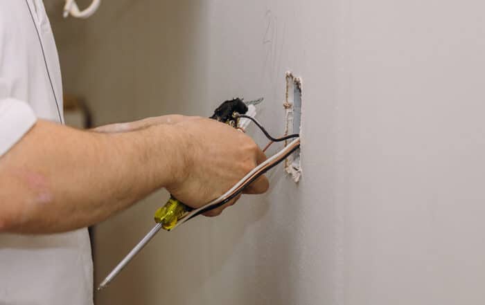 Man cutting wires protruding from a hole in drywall
